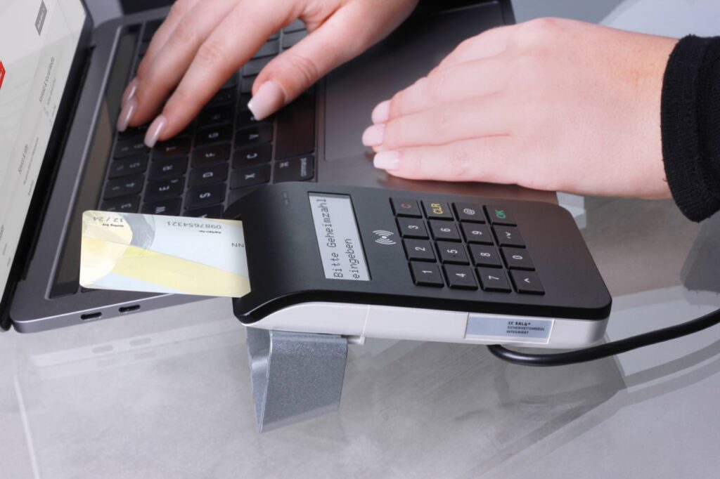 Close-up of contactless payment using laptop and card reader, showcasing modern office technology.